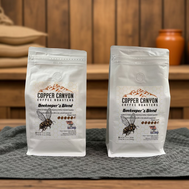 Two white bags of Copper Canyon Coffee Roasters Bookkeeper's Blend coffee placed side by side on a gray textured towel in front of a light gray tiled wall.