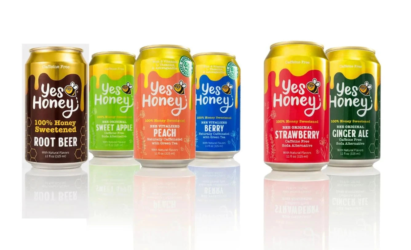 Six Yes Honey craft beer cans lined up on a white reflective surface against a white background. The cans represent different flavors: Root Beer, Sweet Apple, Peach, Berry, Strawberry, and Ginger Ale, each with its own distinct color-coded label.