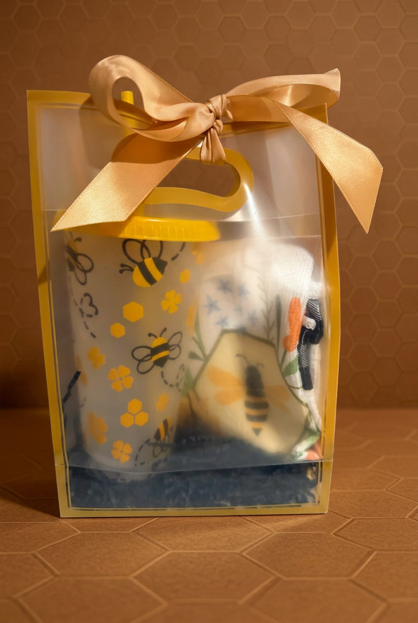 A honey-themed gift set in a clear plastic bag with a gold handle and ribbon, containing a yellow honey pot and a honeycomb-shaped soap, displayed next to a bottle of honey.