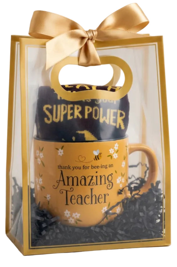 A Teacher Appreciation gift set in a clear plastic bag with a gold handle and ribbon. The set includes a yellow-orange ceramic mug with 'thank you for bee-ing an Amazing Teacher' text, a black and gold 'SUPER POWER' tumbler, and a small jar of honey on a white surface.
